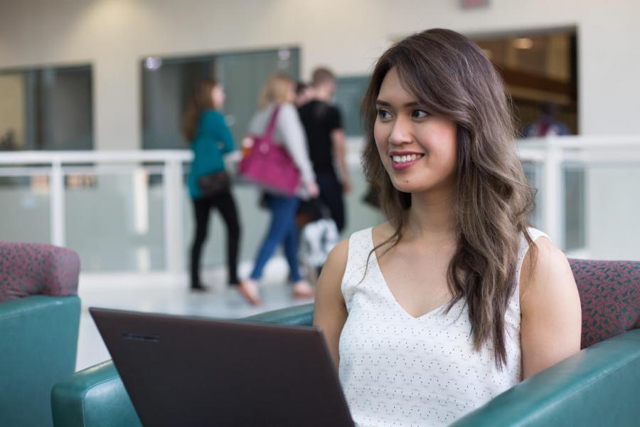 A student sits in a chair working on a laptop in a Bannatyne campus common area.