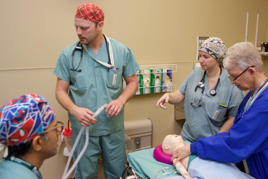Four people work with an infant simulation mannequin. 