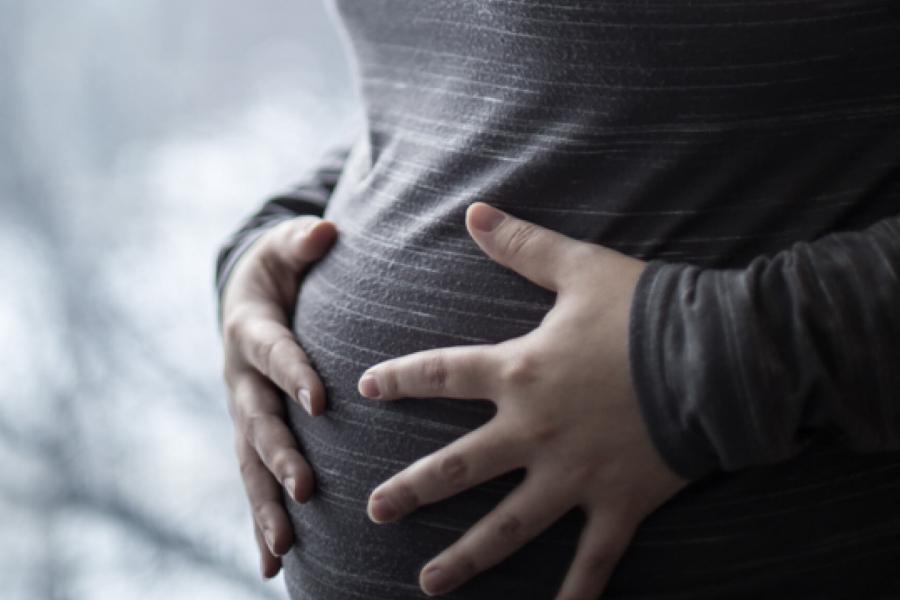 A woman holds her hands over her pregnant belly.