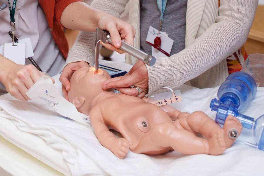 Two people use an infant simulation mannequin to practice their skills.