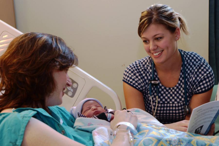 A medicine student sits with a mother and her newborn. 