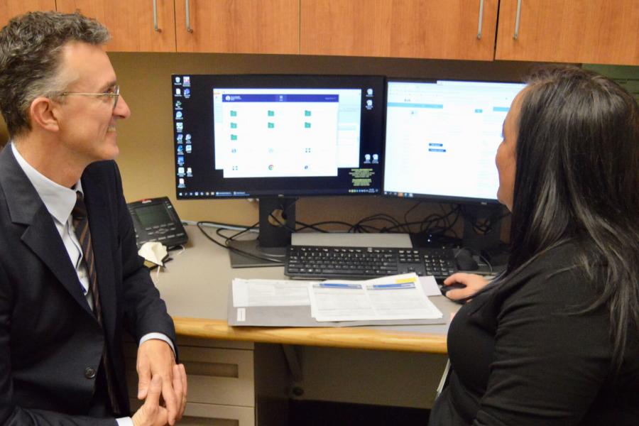 Two medical professionals seated at a desk in an office look at a computer monitor together. 