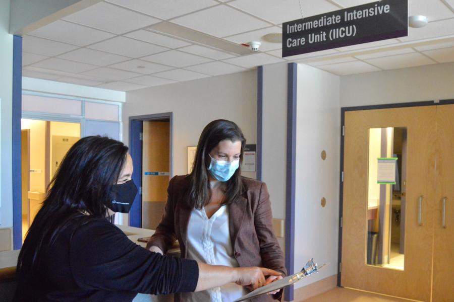 Two medical professionals stand in a hallway speaking to each other.