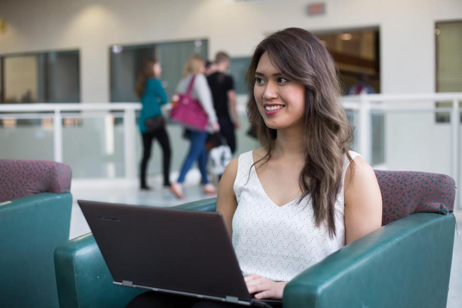 A smiling student is seated in a chair working on a laptop.