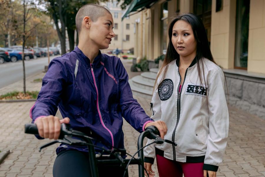 woman with no hair talks to a friend on the street.