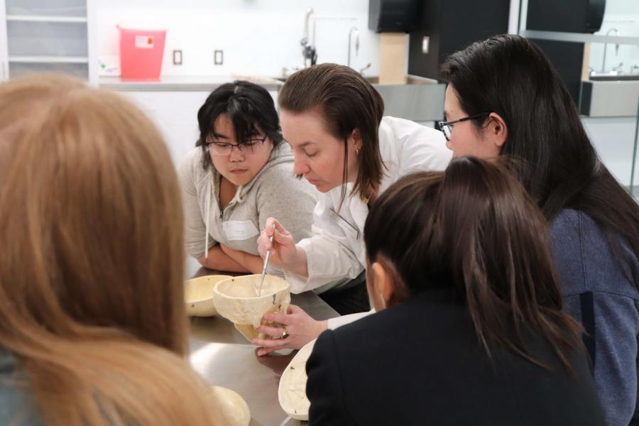 A researcher in a lab coat demonstrating an experiment to a group of high school students.