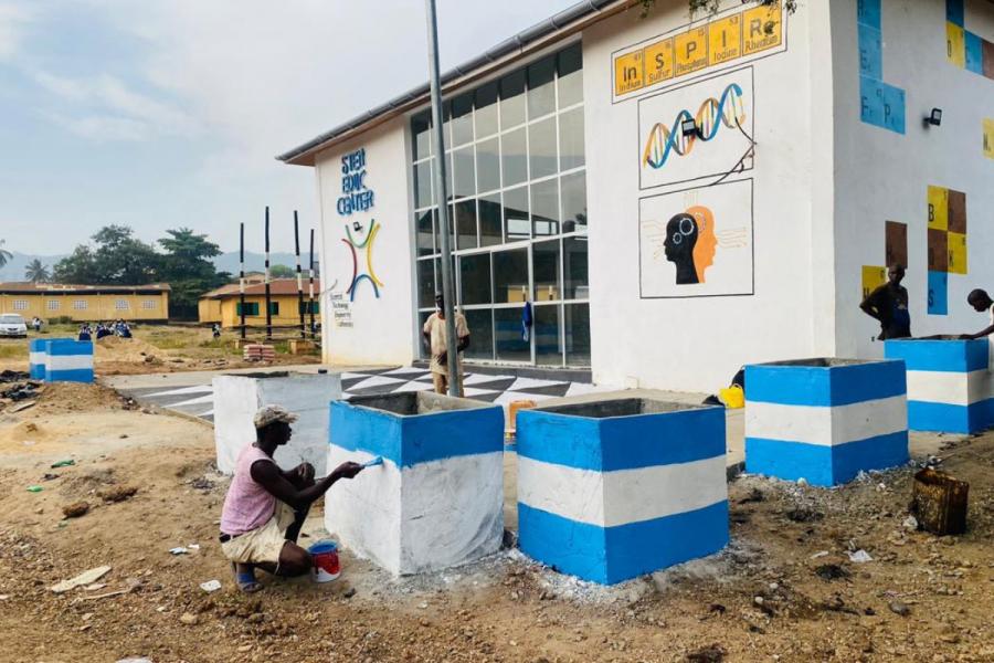 A man painting boxes in front of the STEM Centre in Sierra Leone.
