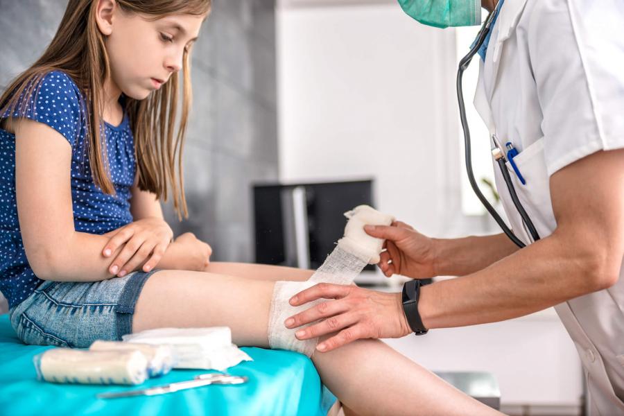Physician bandages little girl's knee.