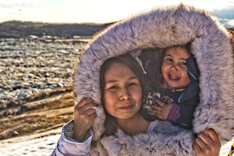 Inuit mother in traditional dress with a baby in her hood.