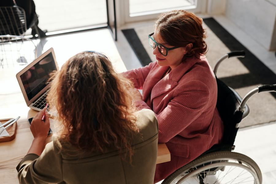 Two people seated at a table, looking at a laptop.