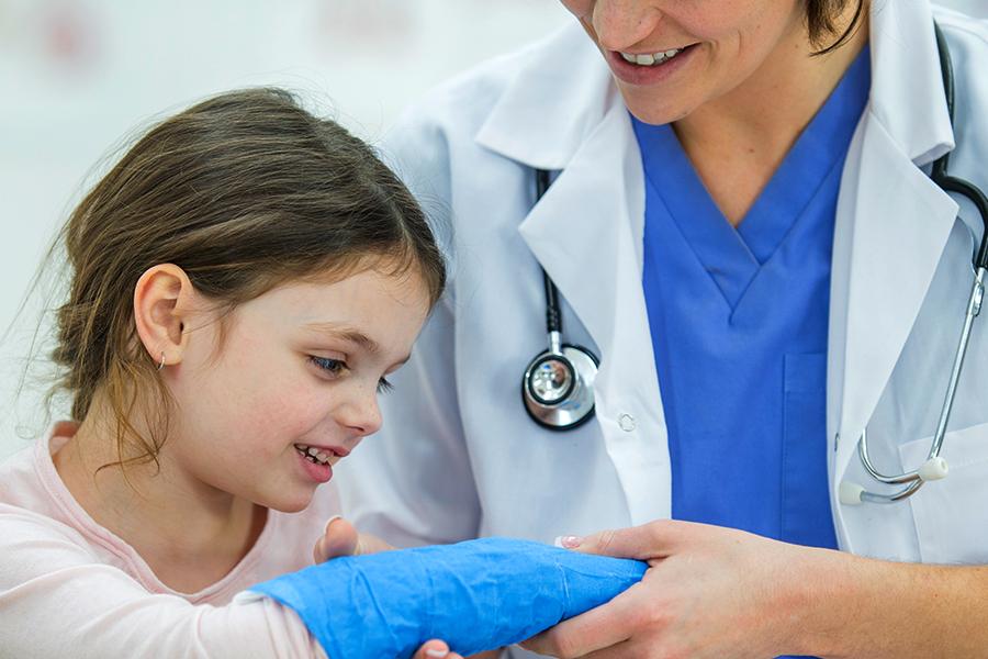 A health professional holds a child patients arm that is in a blue cast.