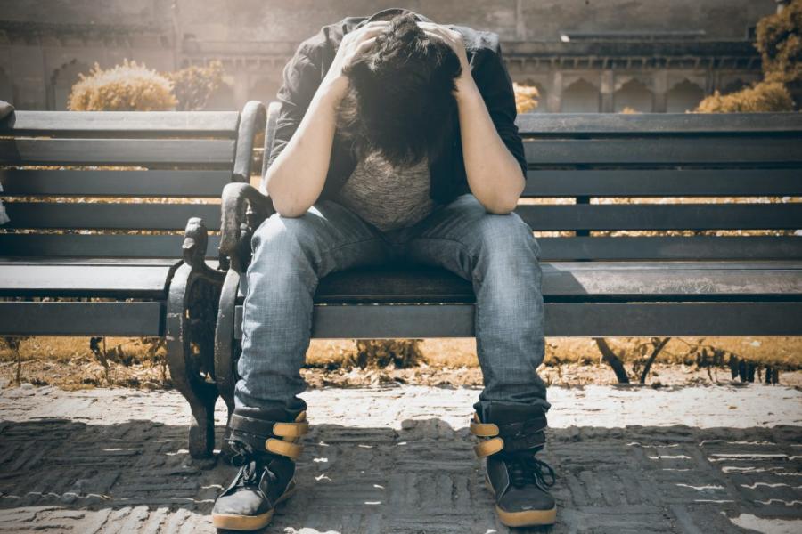 Teen sitting on a bench with his head in his hands.