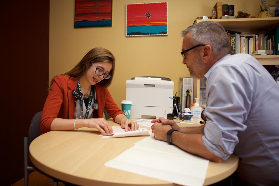 A student sitting at a table, receiving guidance and coaching from a mentor in a collaborative learning environment.