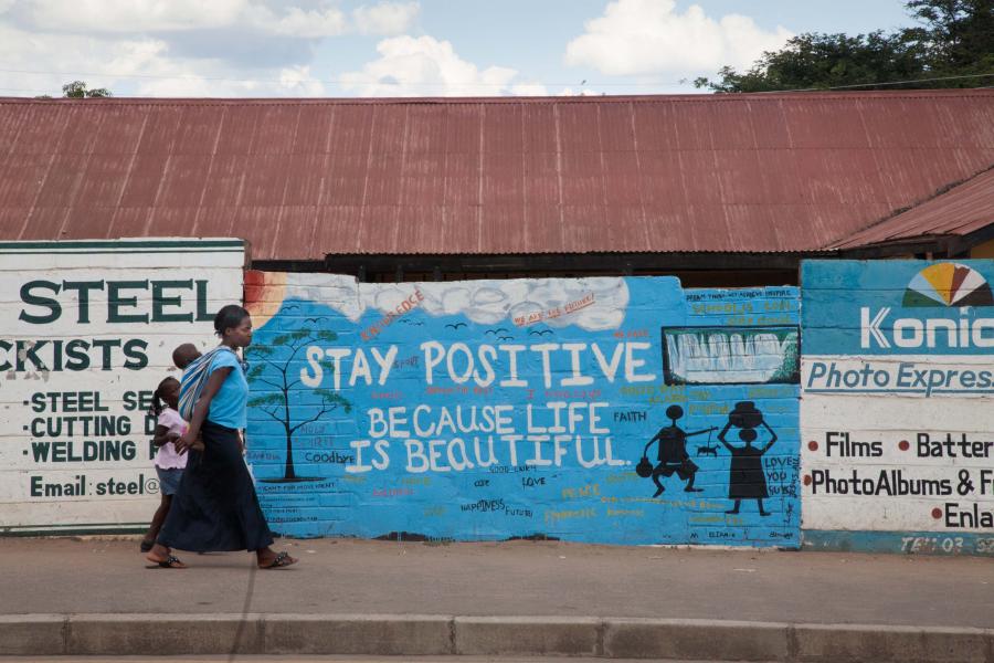 A caregiver walks with two children ona sidewalk in an African village.