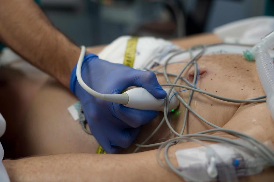 Medical professional performing ultrasound scan on patient's chest area, monitoring vital signs in hospital setting