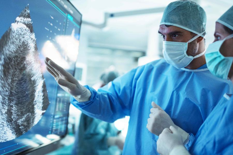 Two surgeons are looking at an ultrasound on a large moniter during a surgical procedure.