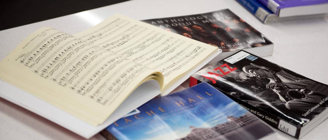 A table top with 6 music related books, one of the books is open to see a spread of pages. 