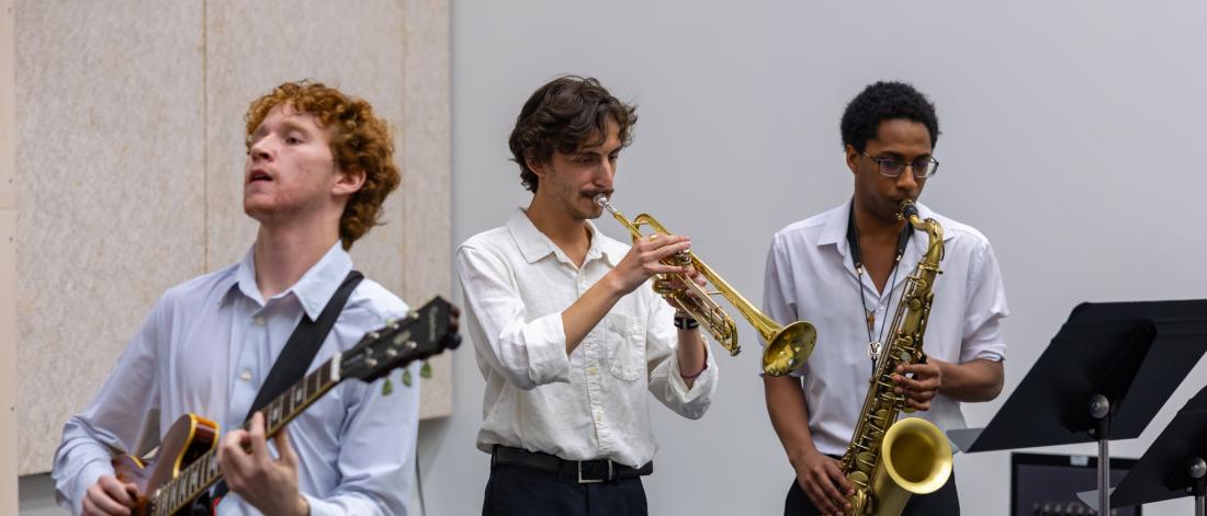 Students playing jazz. From left to right: guitar, trumpet, and saxophone