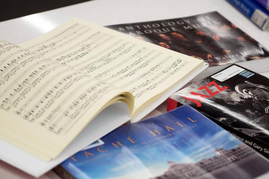 A table top with 6 music related books, one of the books is open to see a spread of pages. 