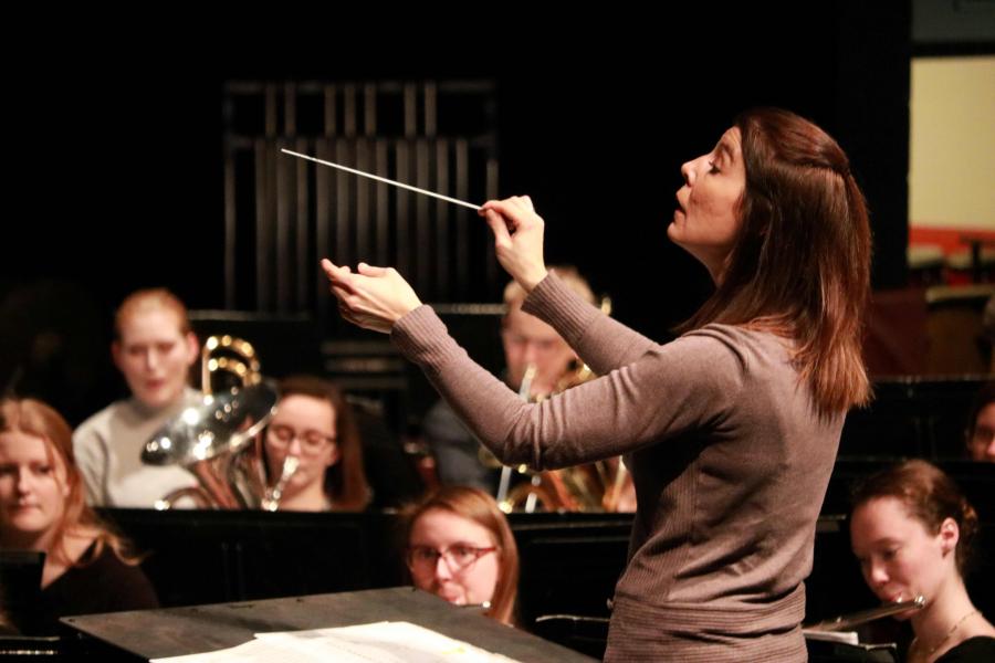 A conductor raises a baton to conduct a wind band.