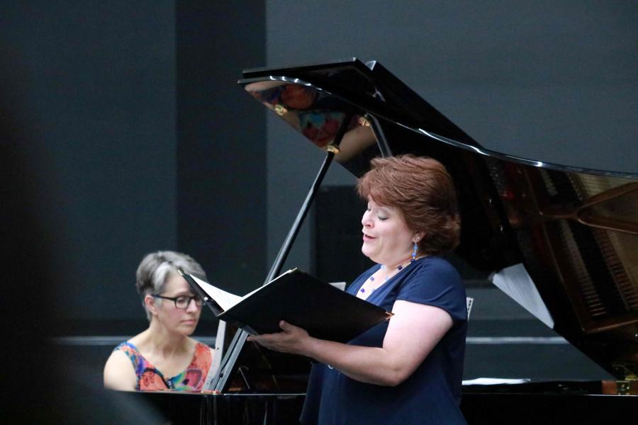 Collaborative pianist Laura Loewen plays piano while a vocalist sings in the foreground.