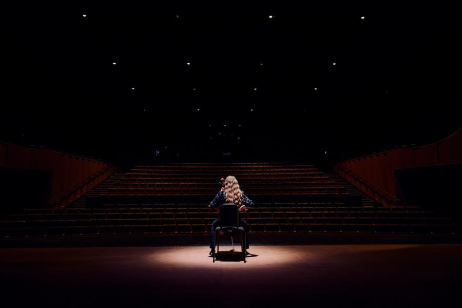 Person illuminated onstage with spotlight, back to the camera playing the cello