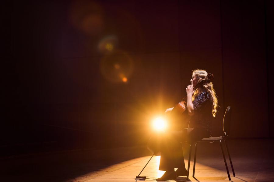 woman illuminated by orange light onstage playing the cello