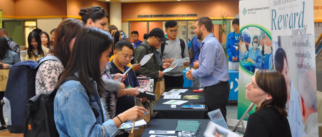 Nursing students gather around a table at an informations session reading brochures about the nursing profession.