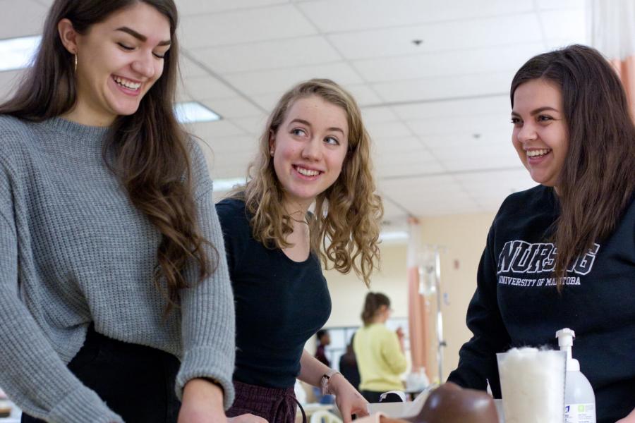 Three smiling nursing students work together in the Nursing Simulation lab.