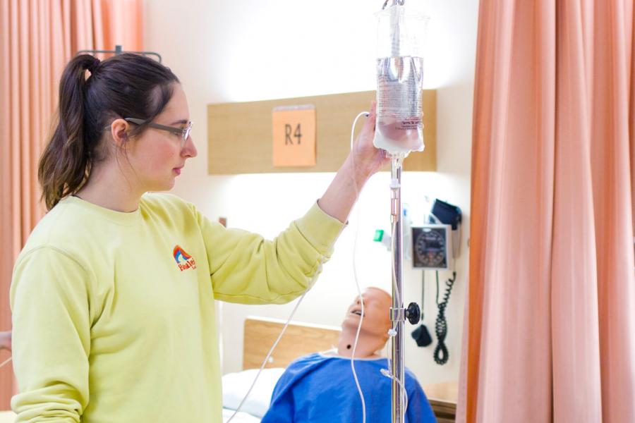 A nursing student works on setting an IV drip onto a pole. 