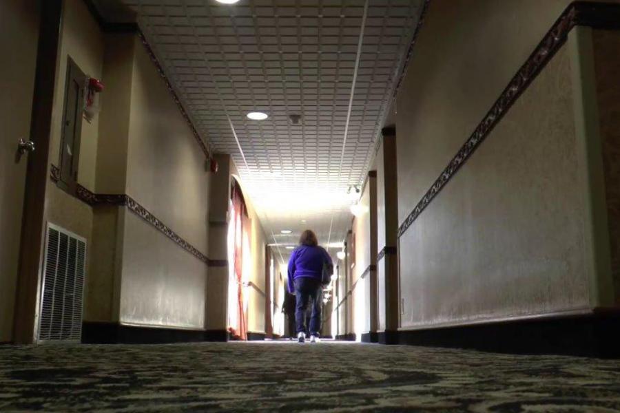 A woman walks down a dark hotel hallway.