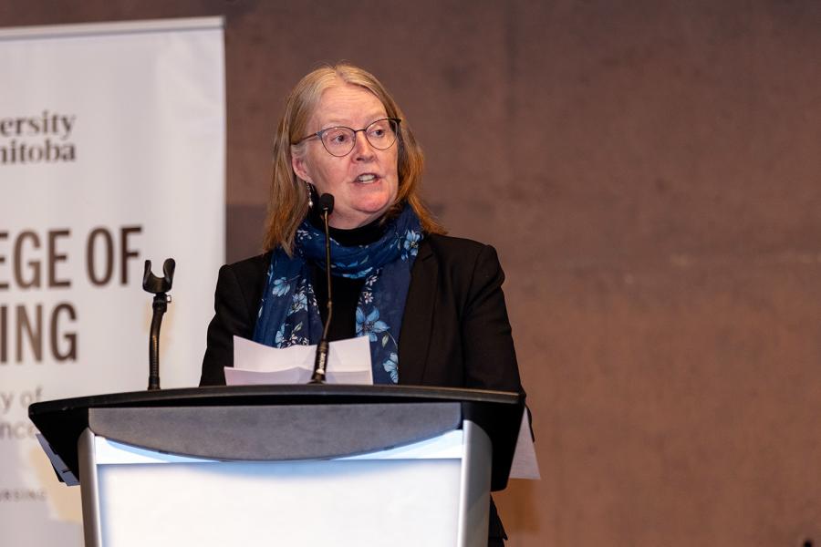Diana McMillan speaks at a podium in front of a University of Manitoba College of Nursing banner.