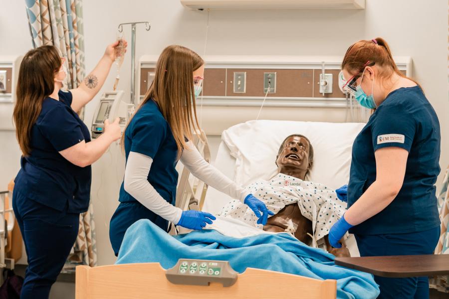 Nursing students working with a manikin in a hospital-style bed in a simulation lab.