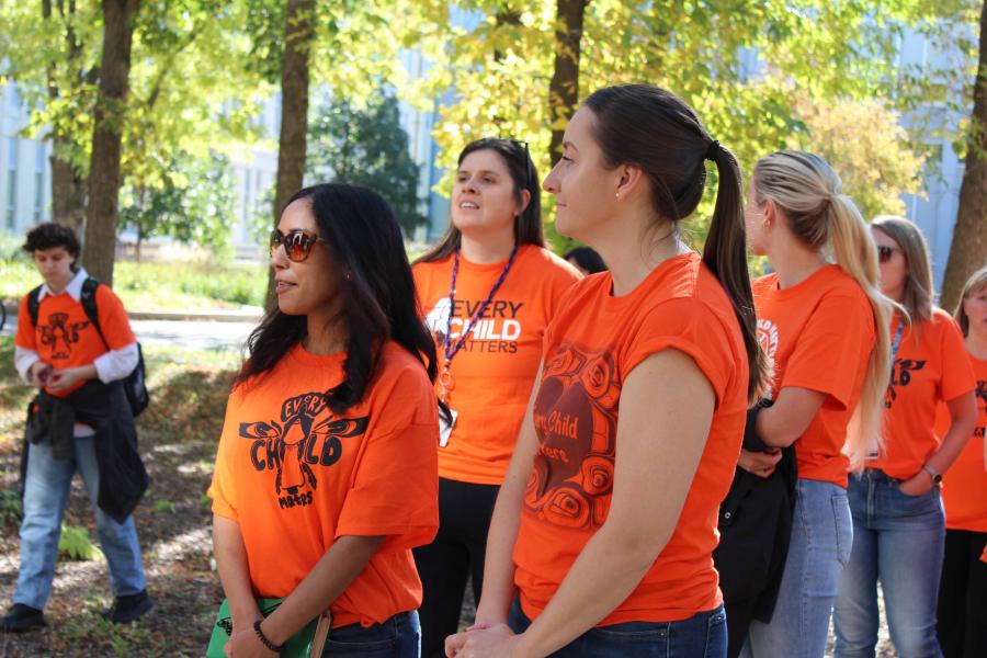 A group of people in orange shirts walking as a group, honouring "Orange shirt day."