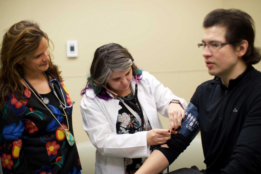 A Doctor supervises a student taking a patient's blood pressure.