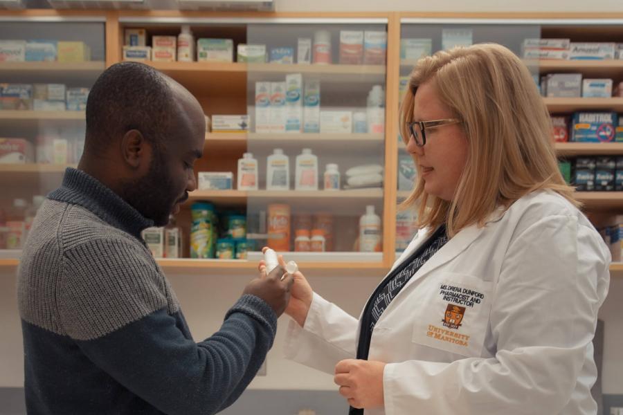 A pharmacist passes an inhaler to a customer while pointing out how to use it. 