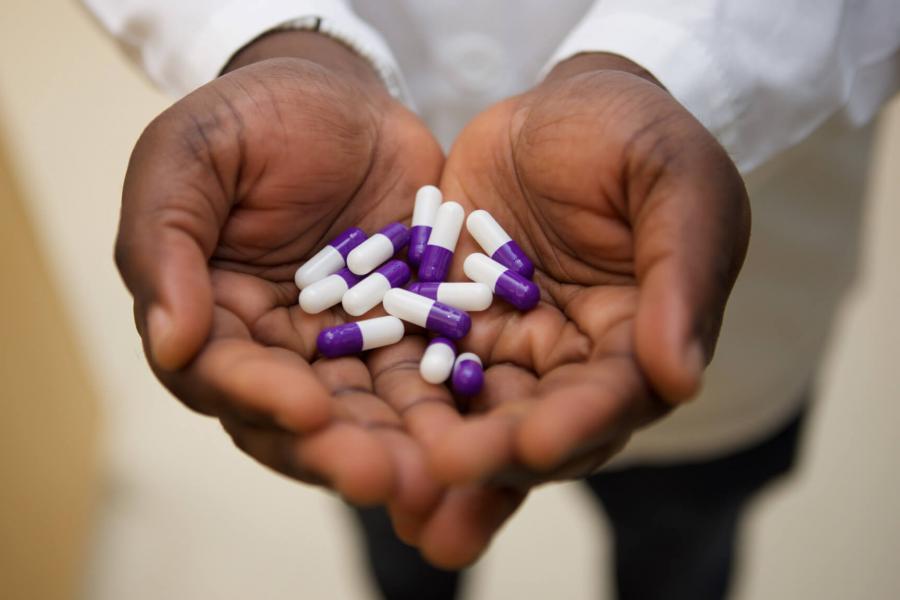 A pharmacist holds his hands out palms facing upwards holding a handful of purple and white pills.