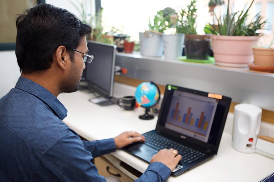 A pharmacy student sits at a desk working on a laptop with a bar graph on the screen.