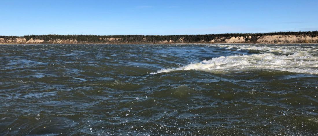 A rapidly moving body of water with a visible shoreline in the distance.