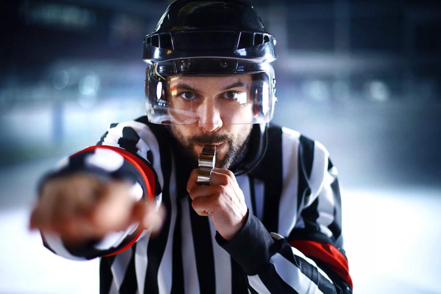 A photograph in which a hockey referee points his finger at the viewer while blowing a whistle.