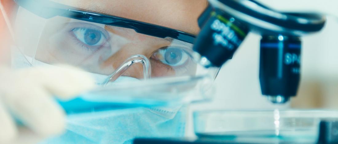 Close up of a scientist with protective glasses working with a microscope.