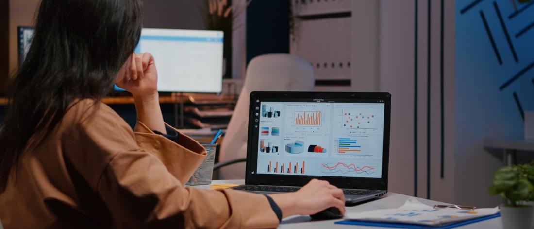 Woman working on a laptop with graphs and data on the screen.