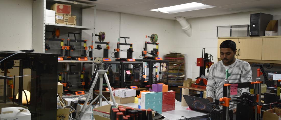 Student in the Maker Space surrounded by 3D printers and 3D prints.
