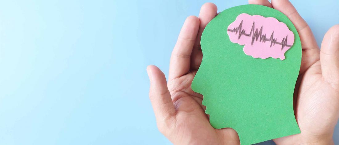 Two hands holding a green paper in shape of a side profile with a pink piece of paper in place of the brain.