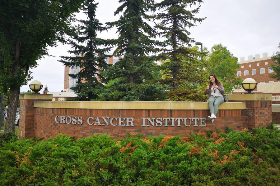 Jennifer Simone sitting at the edge of the sign that reads Cross Cancer Institute