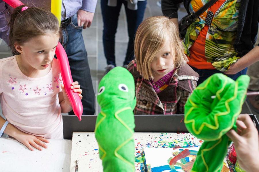 Two kids looking at a plush snake robot that is dancing and painting.
