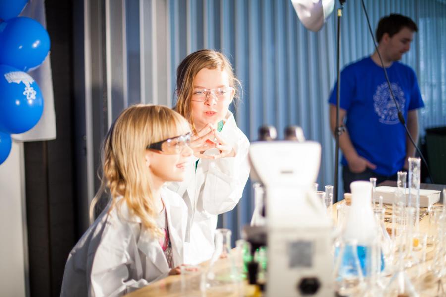Two kids with white lab coats and protective glasses pose for the camera.