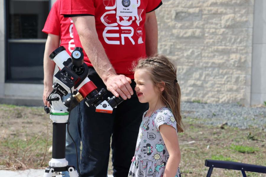 A kid looking into a telescope with the help of a volunteer at Science Rendezvous