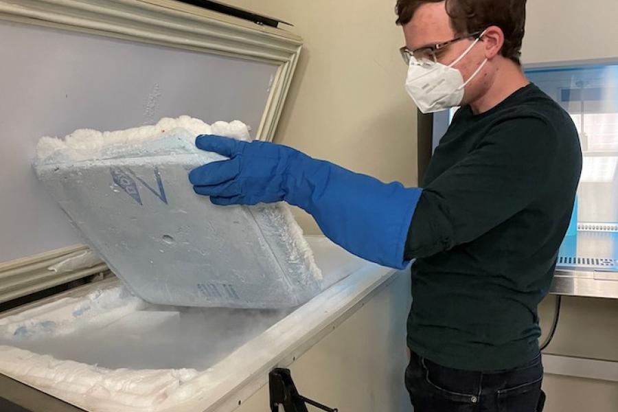 Ben Ulmer Chelikani with gloves and wearing a face mask holding an square styrofoam.