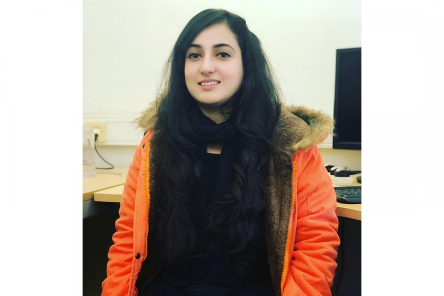 Hina Shaheen wearing an orange jacket and looking at the camera with a smile.